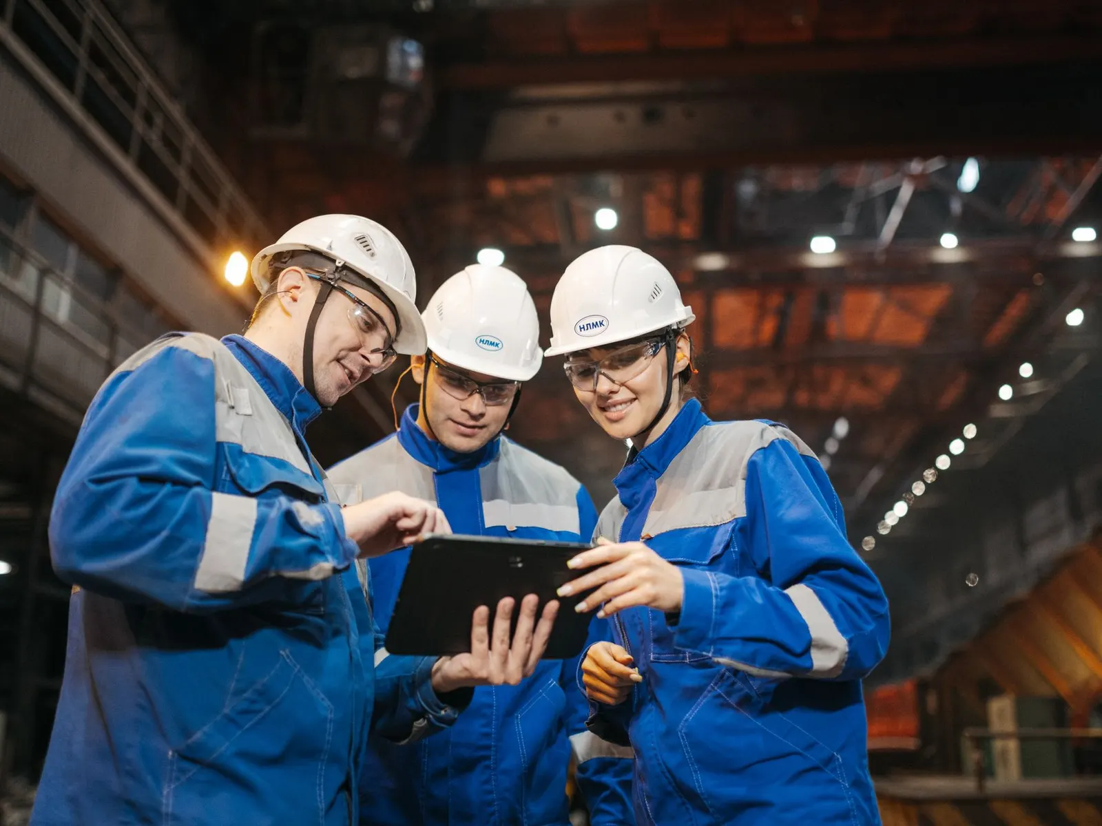 Three engineers in hard hats reviewing a tablet on a factory floor